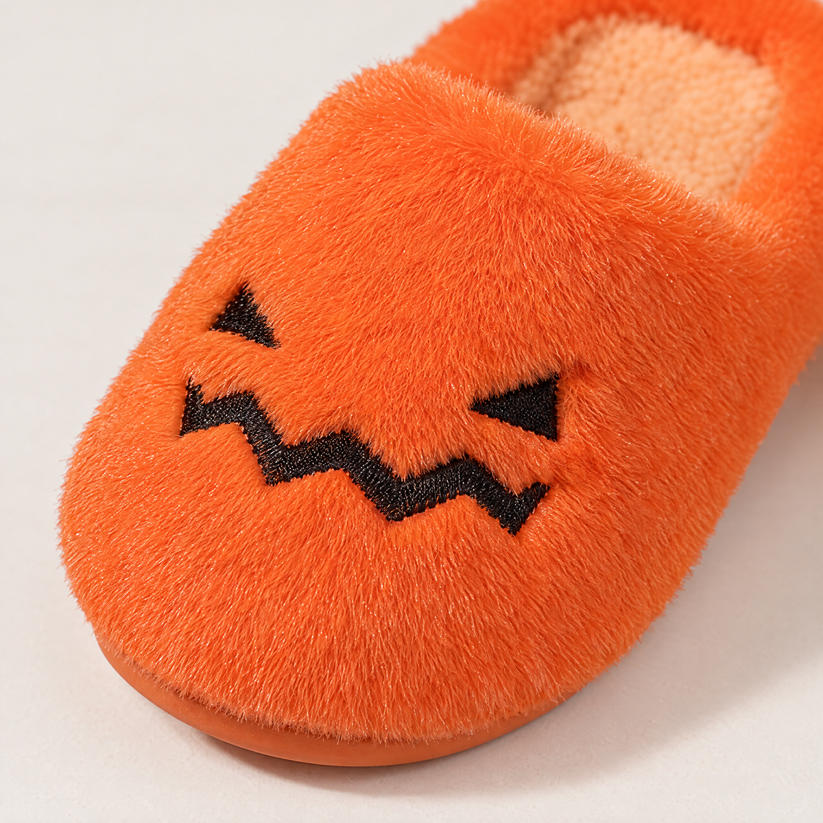 Close-up of plush fur and stitched jack-o'-lantern face on slipper