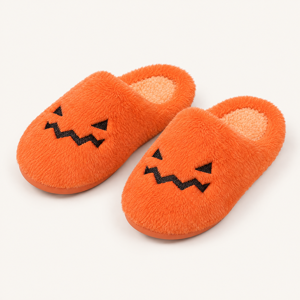 Orange fuzzy jack-o'-lantern face slippers pair, studio shot