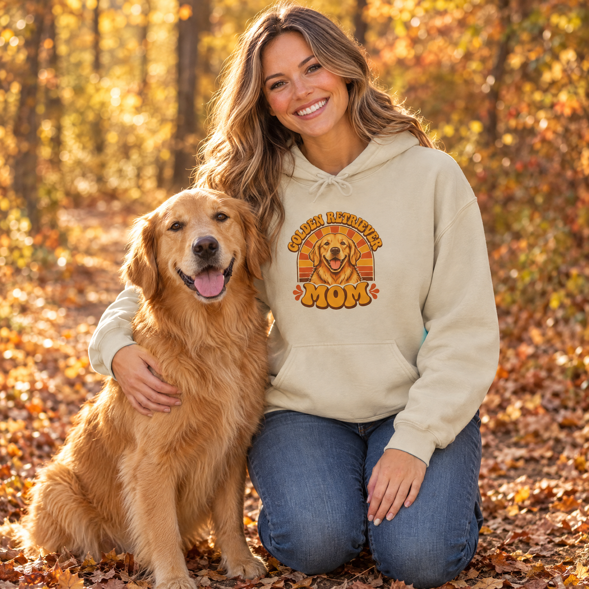 Woman wearing the sand Golden Retriever Mom hoodie kneeling beside her golden retriever on an autumn trail