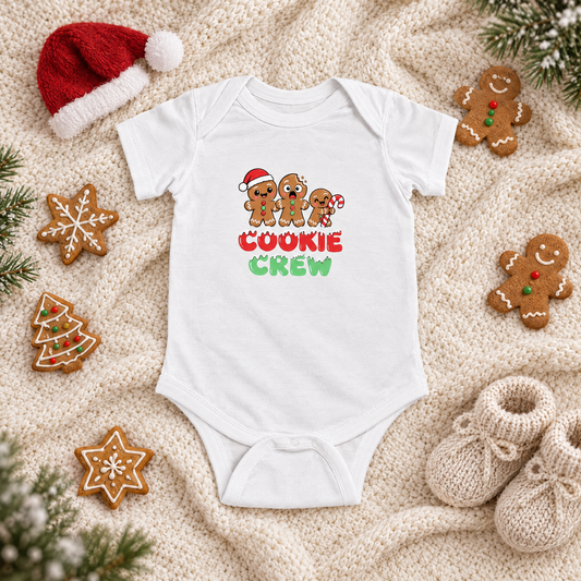White Cookie Crew baby bodysuit flat lay with gingerbread cookies, a tiny Santa hat and knit booties