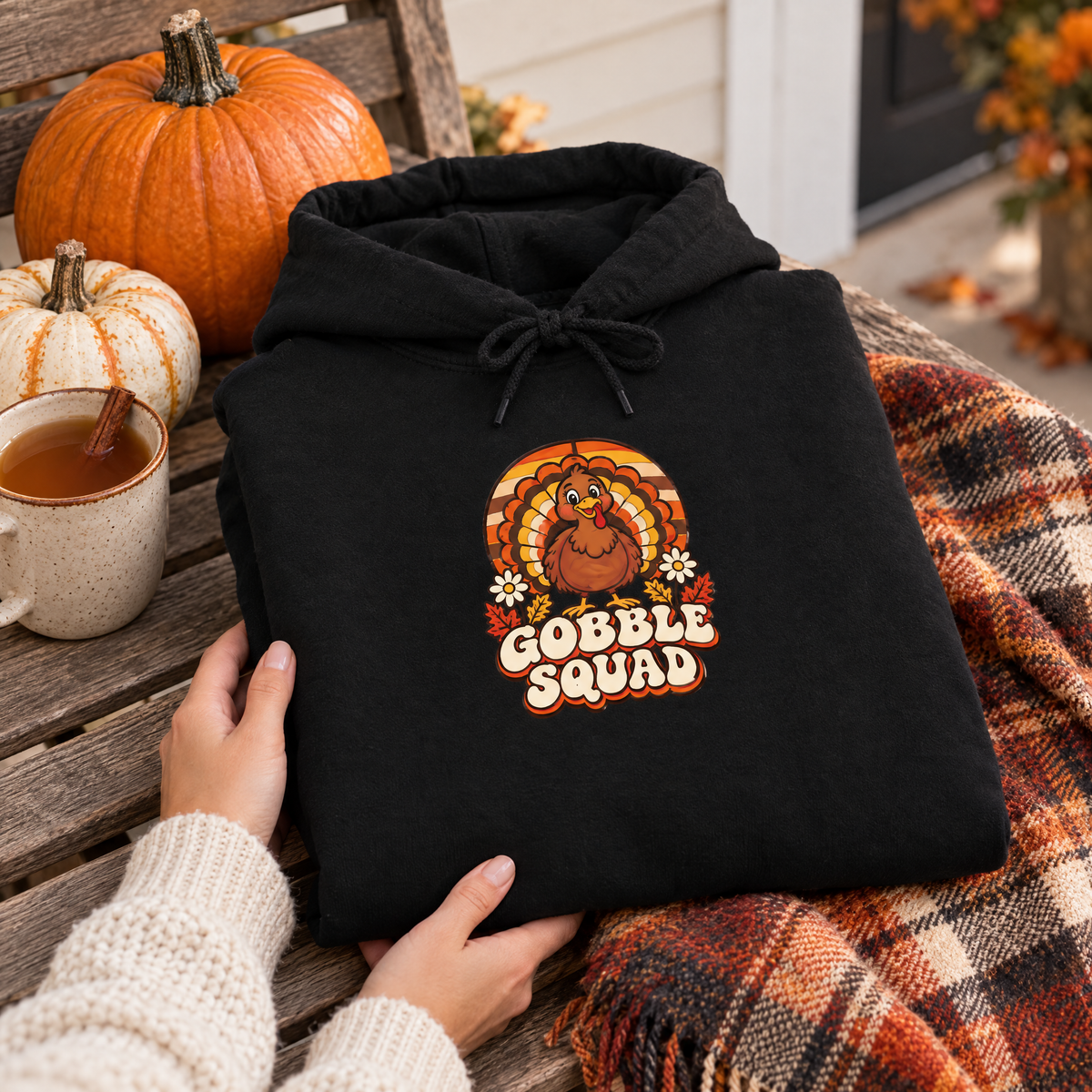 Gobble Squad hoodie folded on a porch bench with pumpkins, cider and a plaid blanket