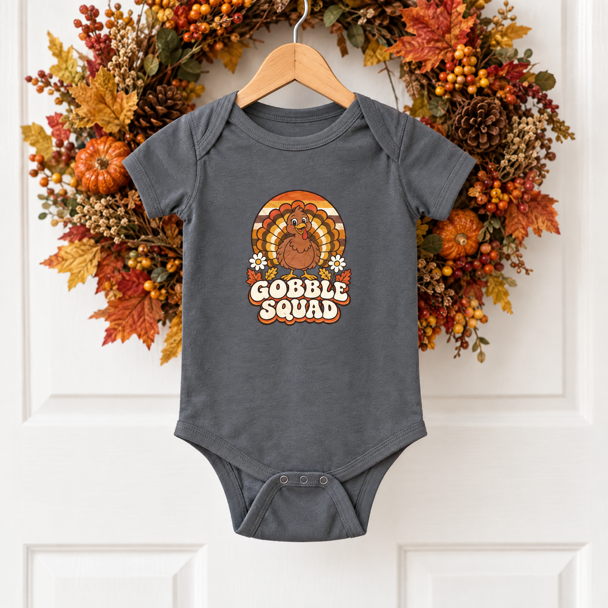 Gobble Squad baby bodysuit on a wooden hanger in front of a fall wreath